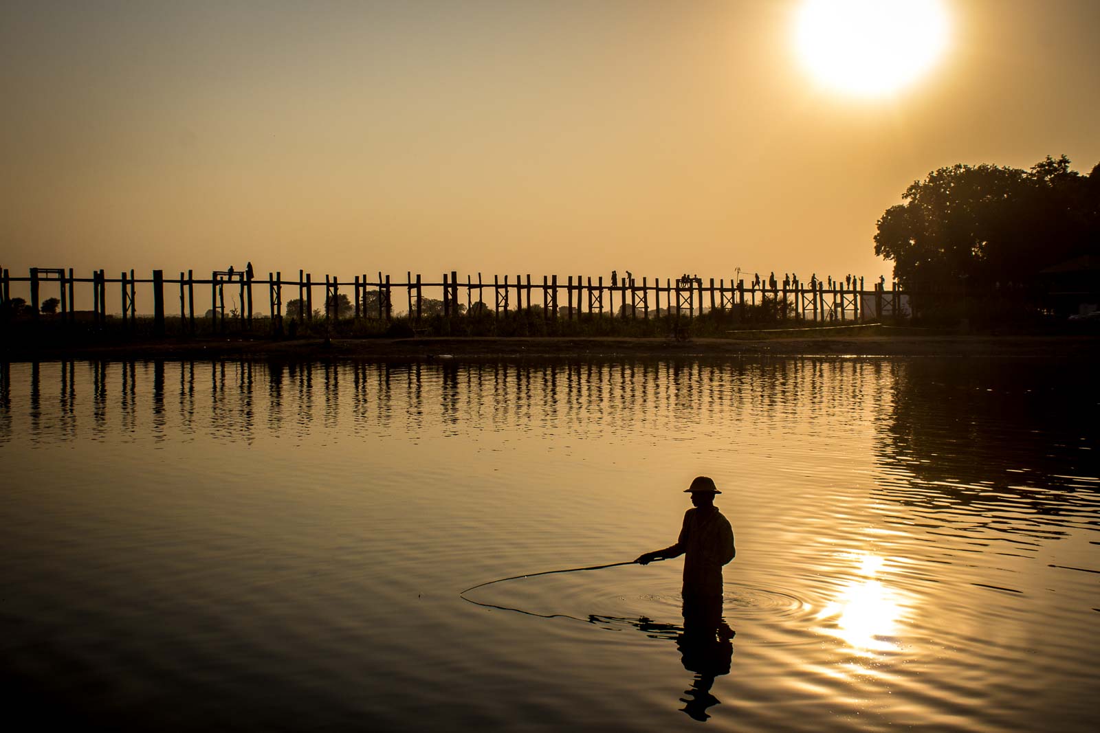 men fishing with triangular scoop net early morning at sunrise near iconic  U-Bein Bridge, on shallow Lake Taungthamanin, Amarapura, Mandalay, Myanmar  Stock Photo